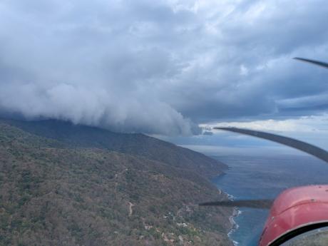 Low clouds gather over the mountains and coastline of Timor-Leste as seen from an MAF flight.